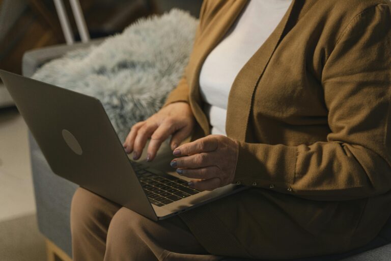 A senior adult using a laptop on a sofa, working comfortably in a home setting.