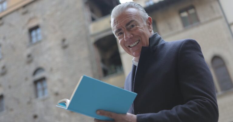 Happy senior man in black coat holding a blue book and smiling outdoors.