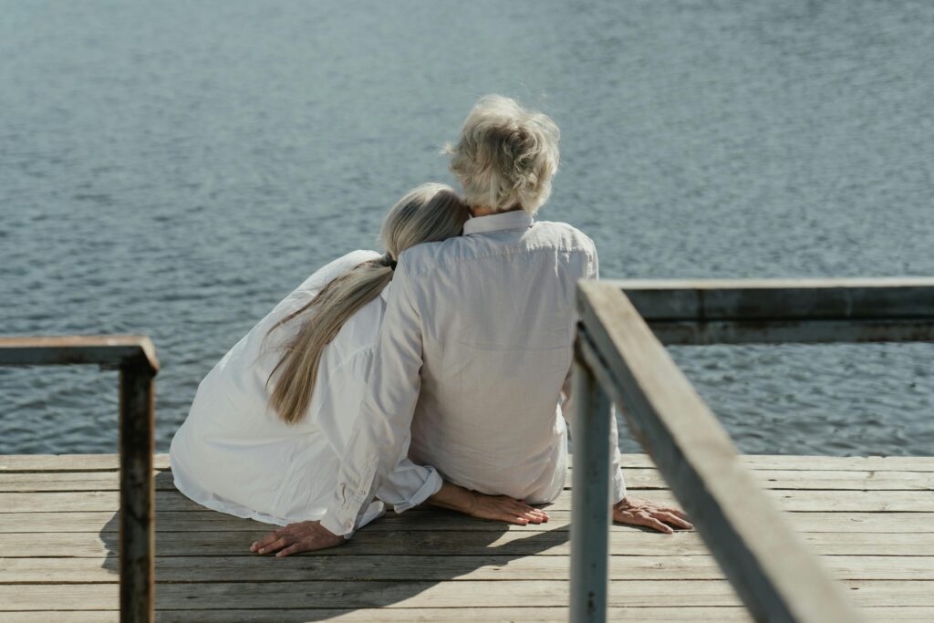 A senior couple enjoys a peaceful moment sitting together on a wooden dock by the lake, symbolizing enduring love.
