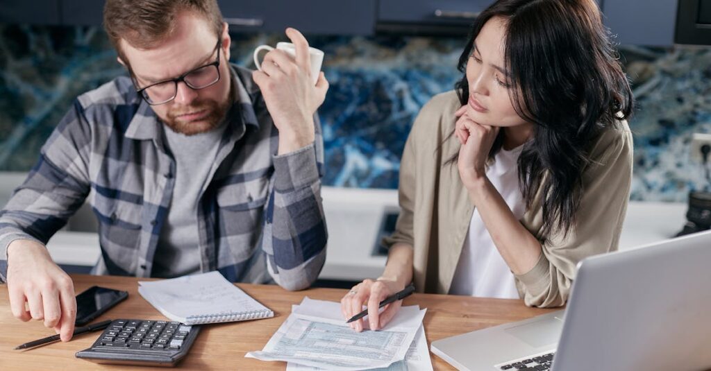 A couple reviews bills and documents on a laptop while discussing household finances.