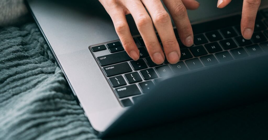 Close-up of hands typing on a laptop keyboard on a cozy home desk setting.