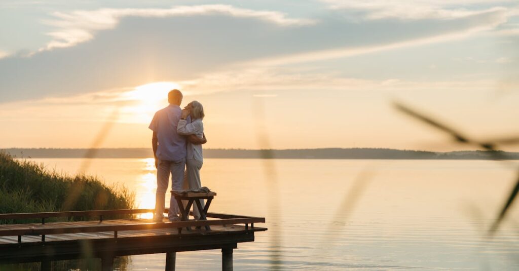 A senior couple embraces on a wooden dock at sunset, exuding tranquility and affection.