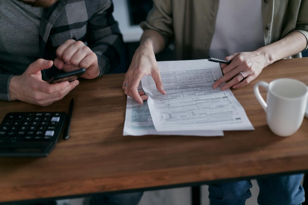 Two adults reviewing financial documents, using a calculator and smartphone at a wooden table.