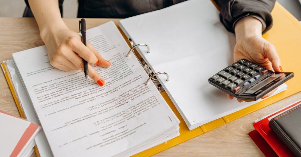 A woman reviewing documents and using a calculator on a wooden table.