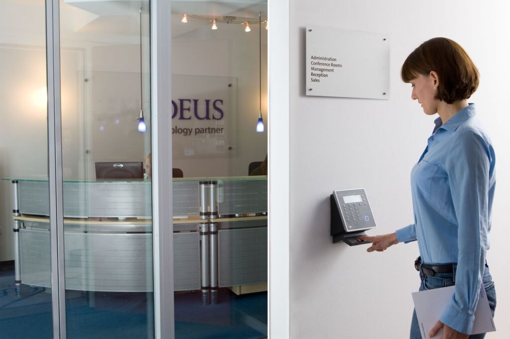 Woman using biometric scanner in modern office setting for access control.